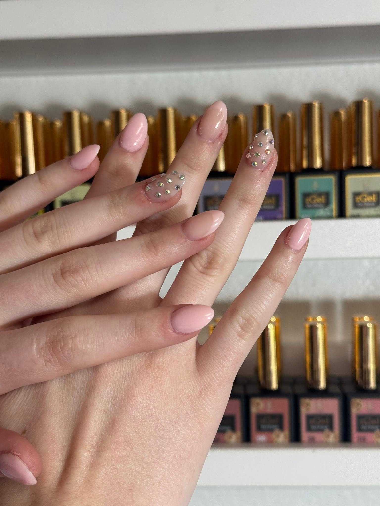 Nude manicure with two accent nails covered in crystal rhinestones
