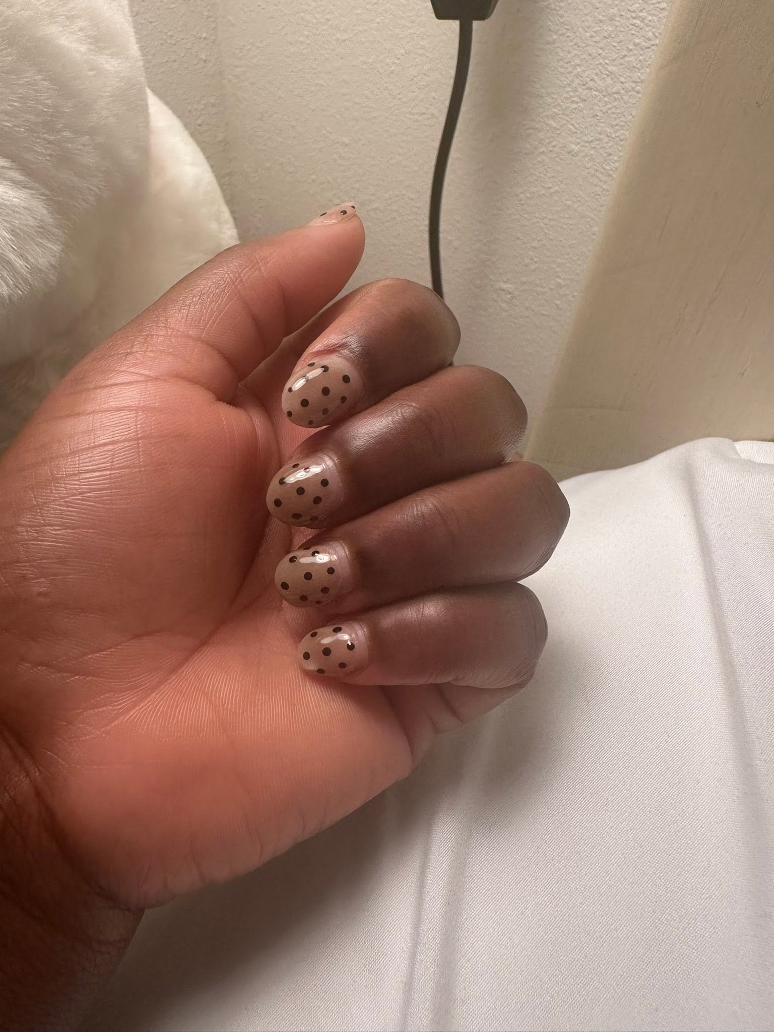 Nude manicure with black polka dot nail art on almond nails